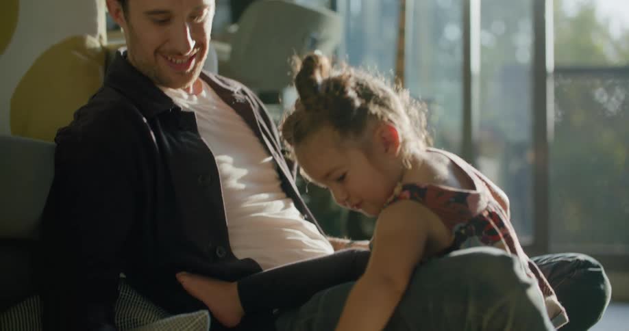 Father and daughter sit on floor in living room while she draws with marker
