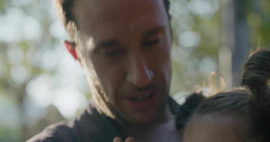 A man holding and hugging a little girl with trees the sky and clouds in the background