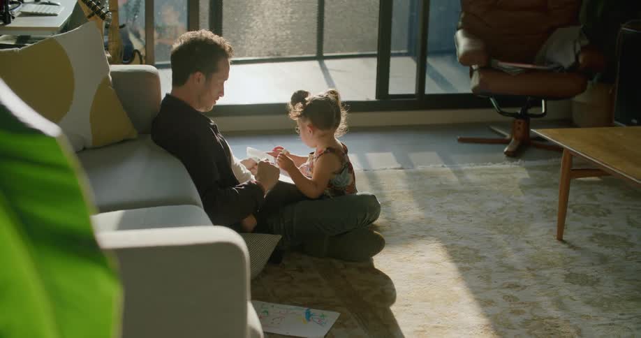 A man sits on the floor playing with his toddler daughter