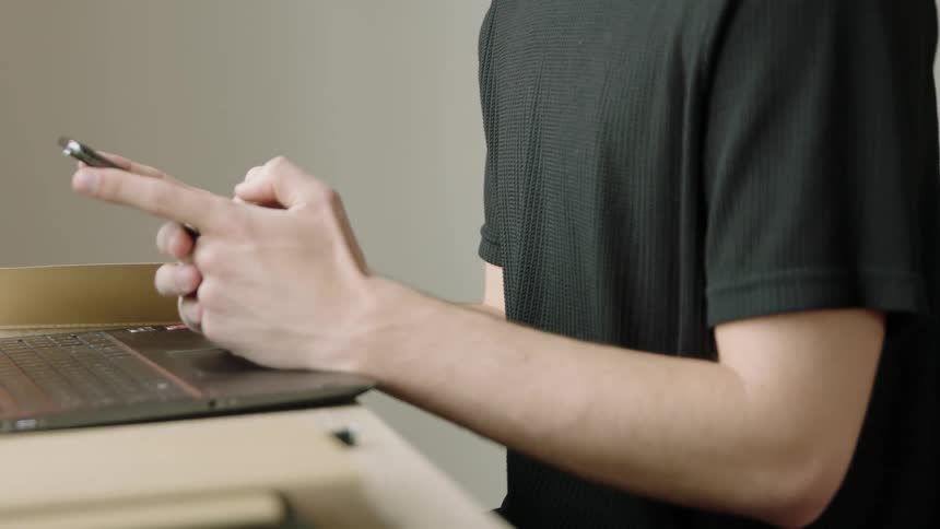 Man sitting in front of laptop views mobile phone