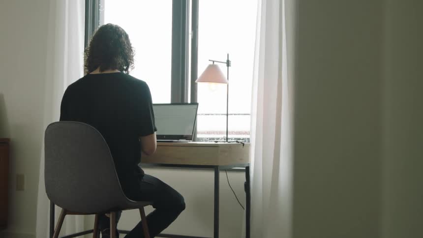 A person uses a laptop at a desk while a dog rests on the floor beside them