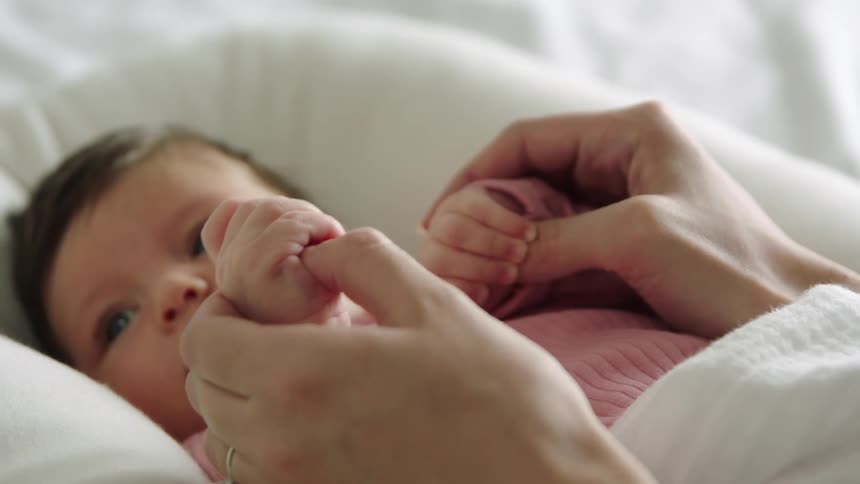 A mom holds her baby daughters hands