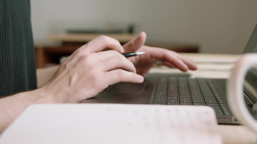 Hands scrolling on a mousepad of a dark grey laptop computer at a desk indoors