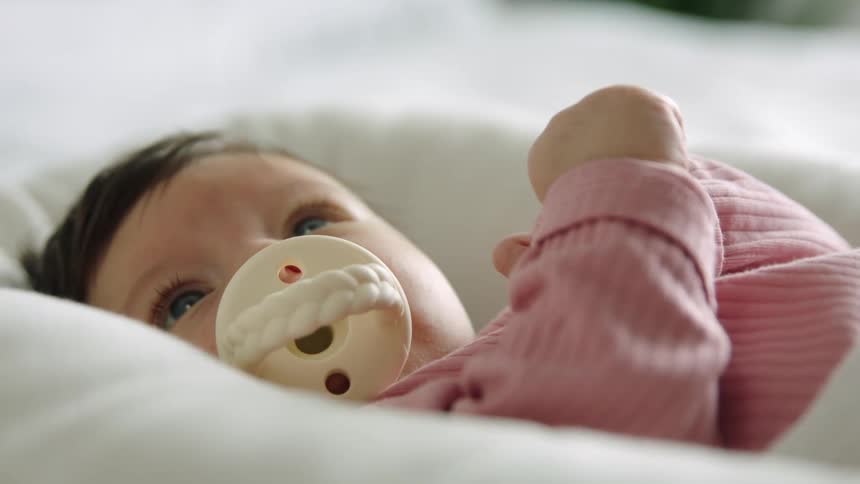 A baby lies in a bed with a pacifier in its mouth