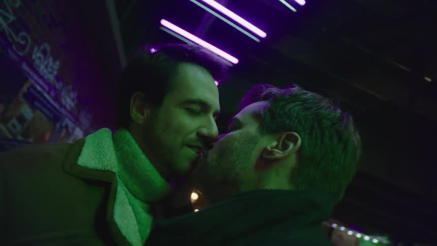 Two men smiling and kissing in the dark