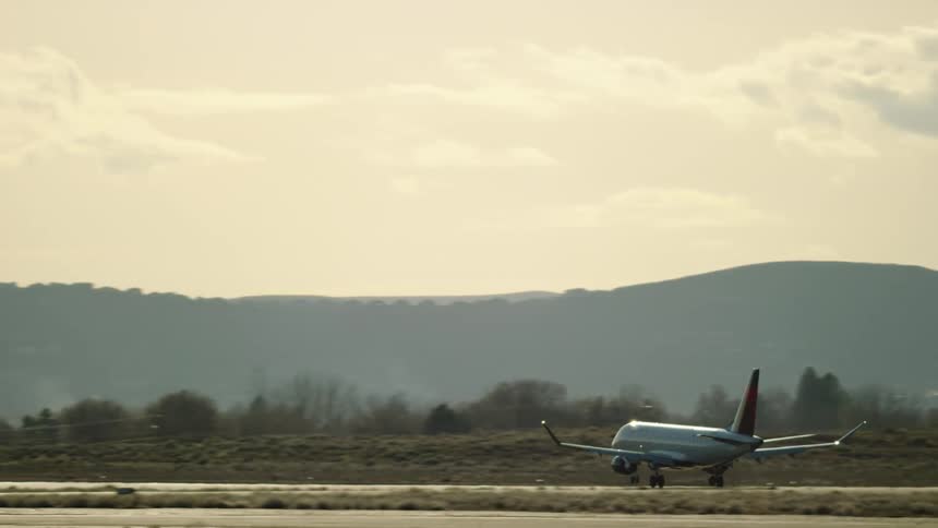 A Embraer E175 Commercial passenger jet airplane lands at an airport in warm afternoon light