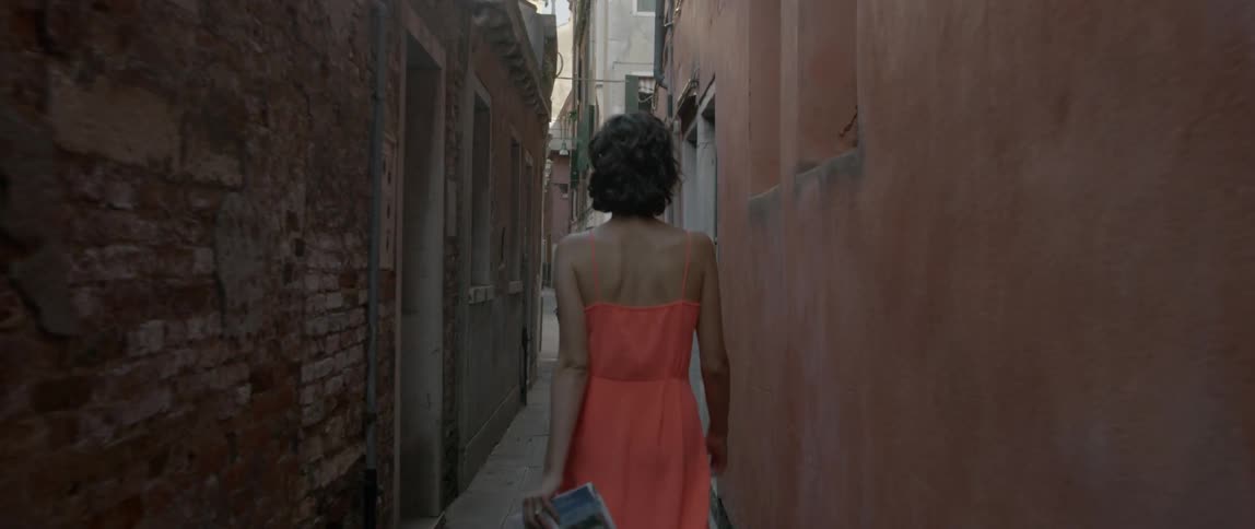 A woman wearing an orange dress walks through a narrow alleyway