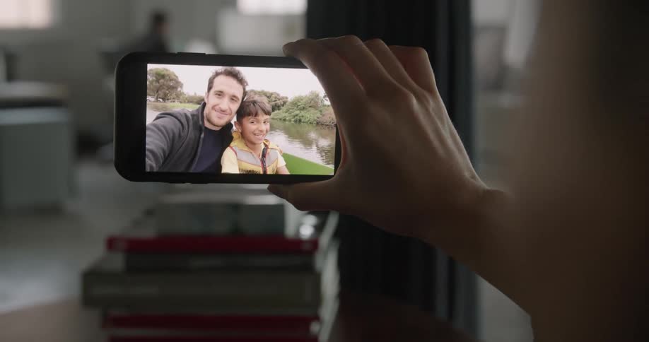 A father and son smiling while video chatting with a woman