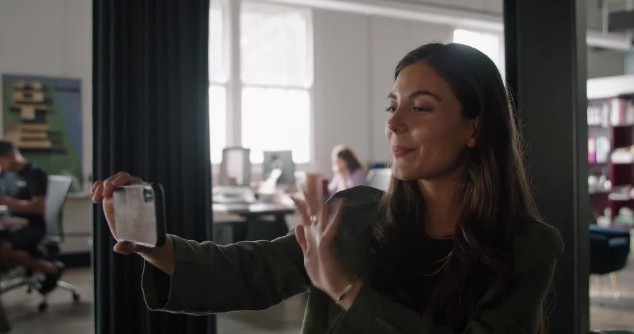 A woman in a room using a smart phone with people and desks in the background