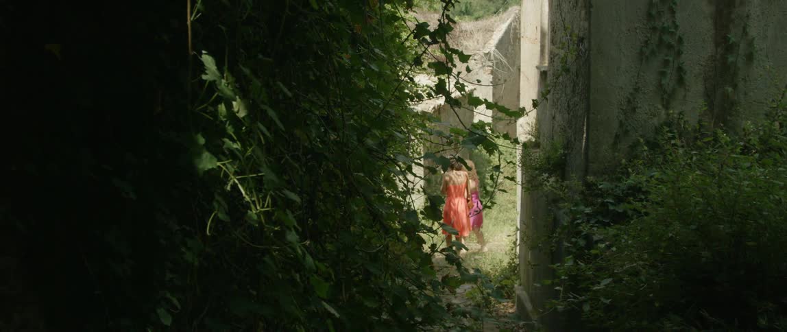 Two women are walking near an ivy covered wall