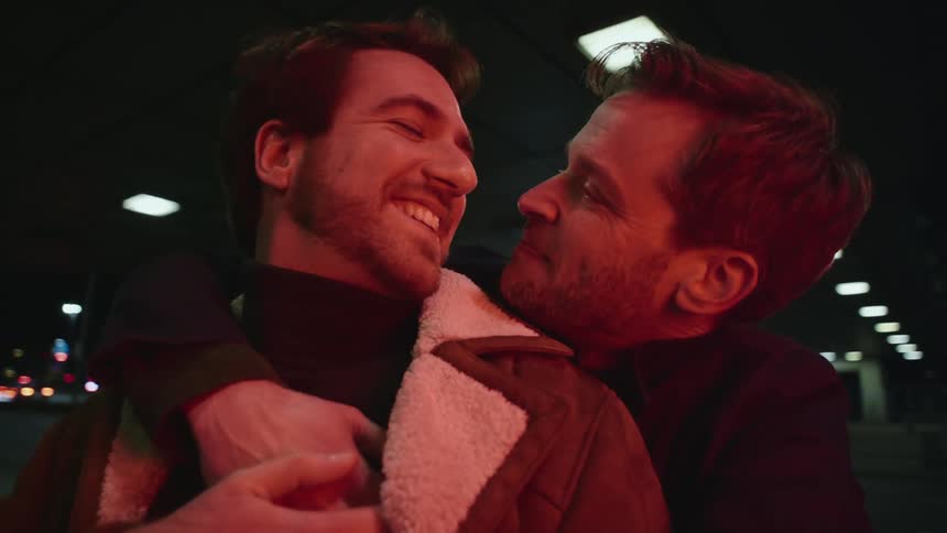 A man hugs his boyfriend from behind as they kiss near a downtown tunnel as vehicles pass by