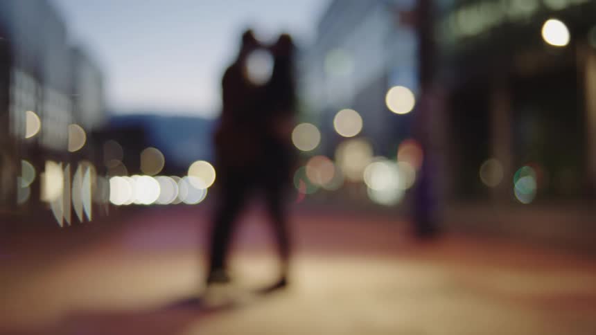 Two silhouetted people kissing on a city sidewalk at night