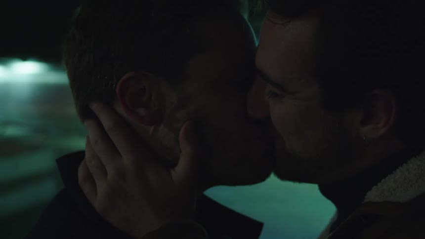 A man lovingly touches and holds his boyfriends face as they kiss and smile at each other