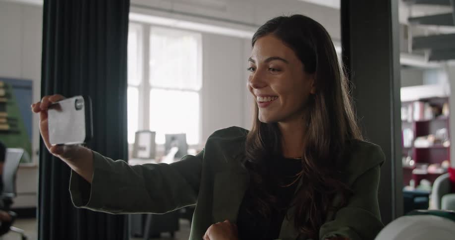 Woman working at the office greets someone on a video call in her smartphone