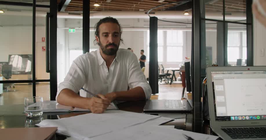 A man sitting at a desk with laptops while holding a pencil