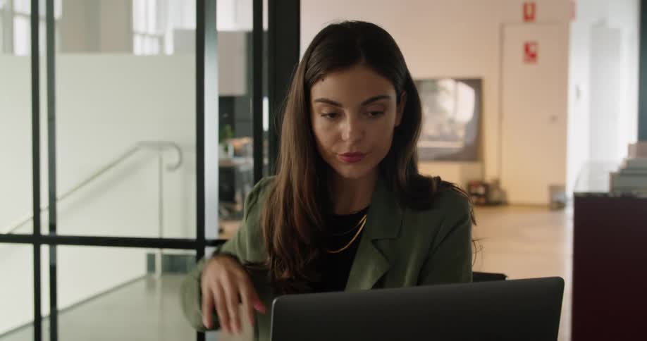 A woman sitting on a chair at a desk typing on a laptop