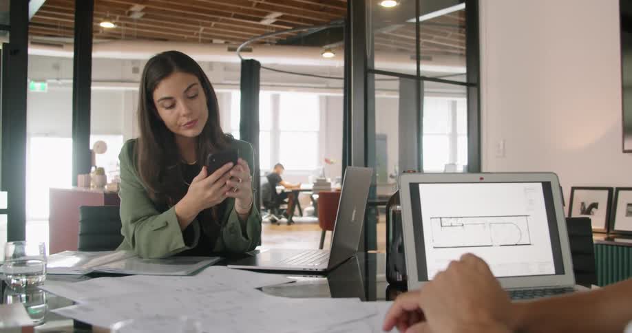 A woman and a man at a desk with laptops looking at a smart phone