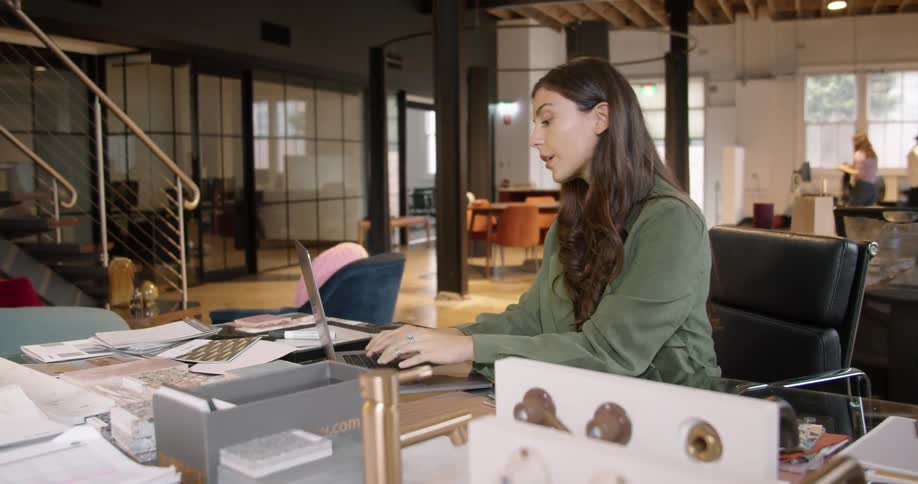 A woman sits with her chin resting on her hand then begins to type on her laptop