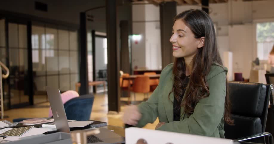 A woman sitting on a chair at a desk video chatting on a laptop
