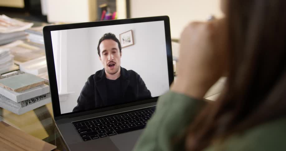 Woman with brown hair and green sweater makes a video call on her laptop