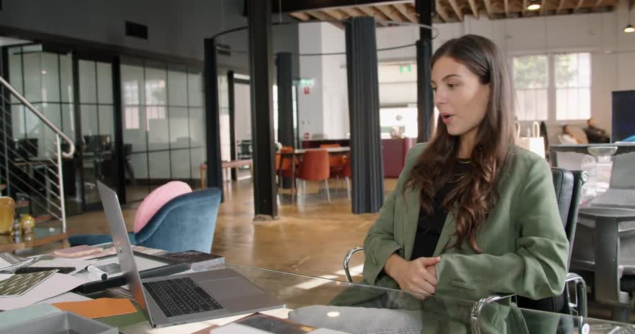 Woman working at the office greets someone on a video call in her laptop