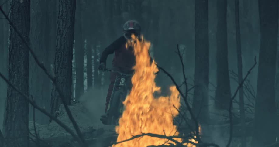 A person wearing a helmet rides a mountain bike towards burning flames in a forest