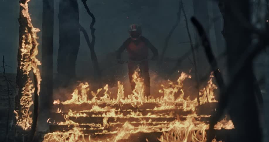 A person rides a mountain bike down flaming logs in a forest fire