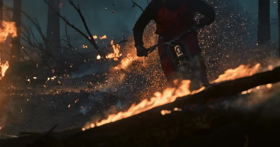 Mountain biker riding through burning forest with explosion of sparks behind them.