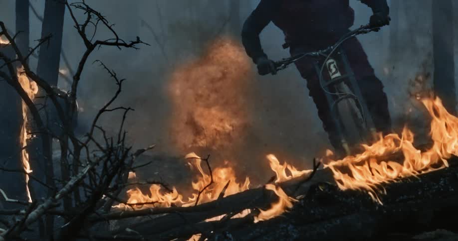 Mountain biker riding through. burning forest with fireball behind them.