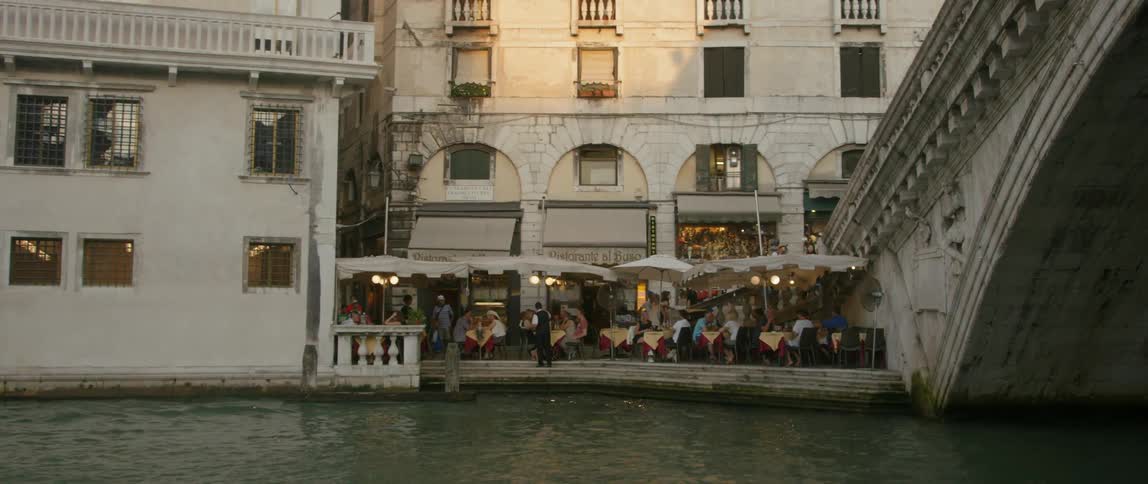 People dining outside of a building next to a manmade river