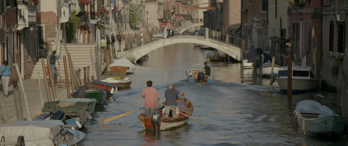 People are rowing and steering boats in a canal