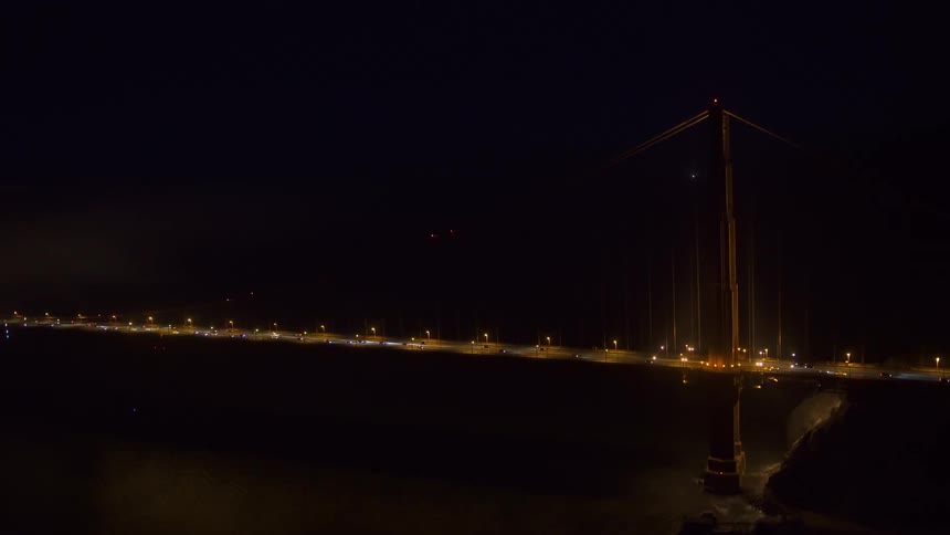 Aerial view of traffic flowing on a suspension bridge over a river at night