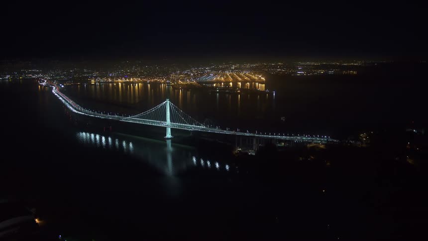 Aerial view of a suspension bridge over a river near a waterfront city at night
