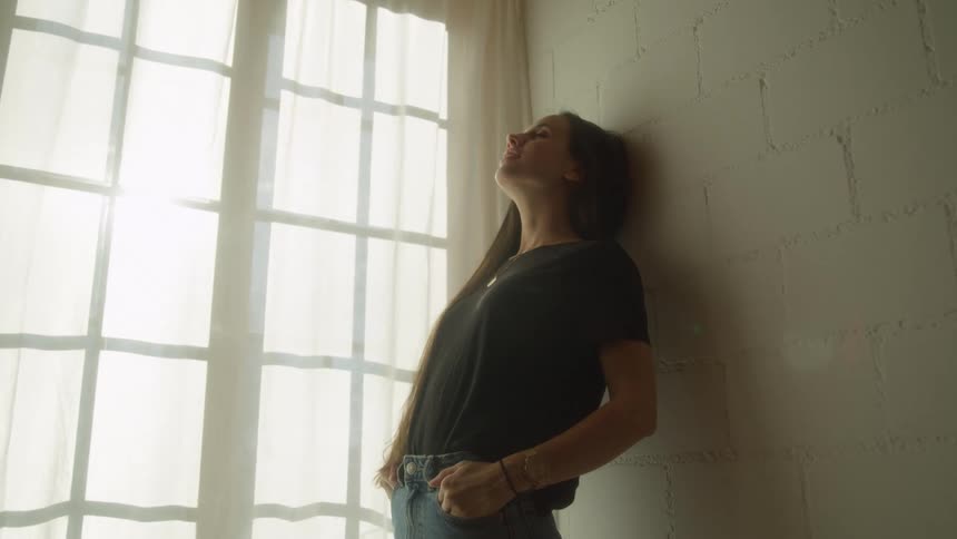 Young woman reclined on a wall brick wall near the curtains on a window