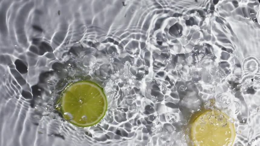 Two lemon slices sliding over water on a white background