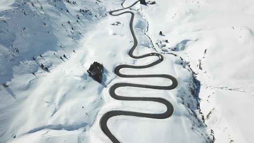 Aerial of vehicles traveling on a winding road through snow covered mountain