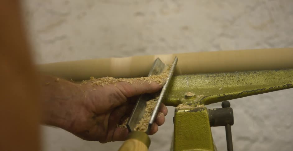 Person shapes turning wooden pole with hand tool