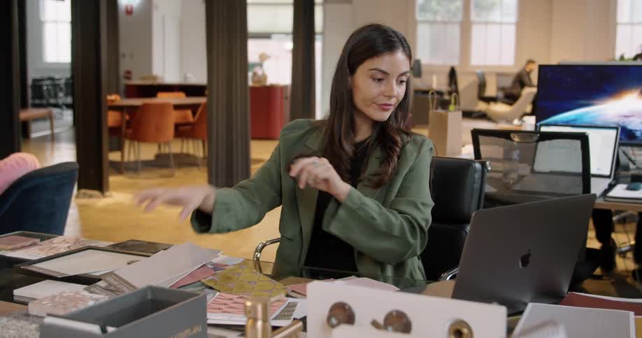Woman sitting at a desk in the office checks samples of products and writes on a laptop