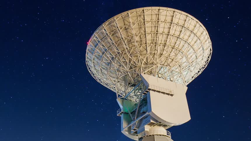 A large satellite dish beneath a starry night sky