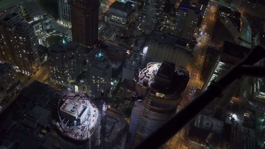 A helicopter flying over a city with building skyscrapers vehicles and streets