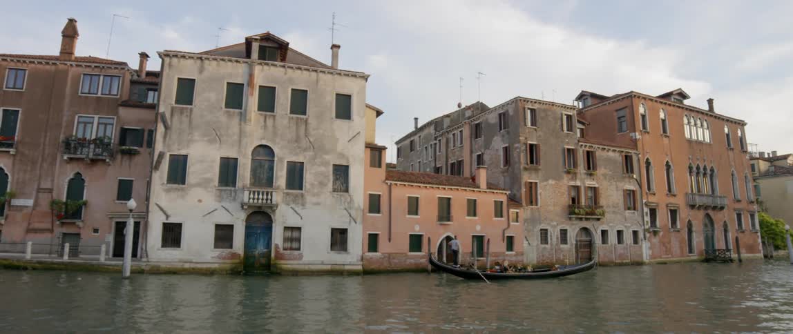 A gondola is oared past old buildings lining a canal