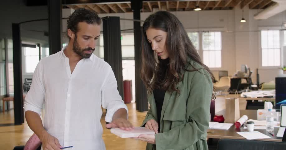 Colleagues discuss stationery options that are spread across a glass table in an office