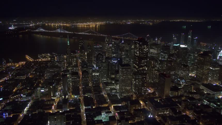 Aerial view of illuminated buildings next to the river with a bridge at night