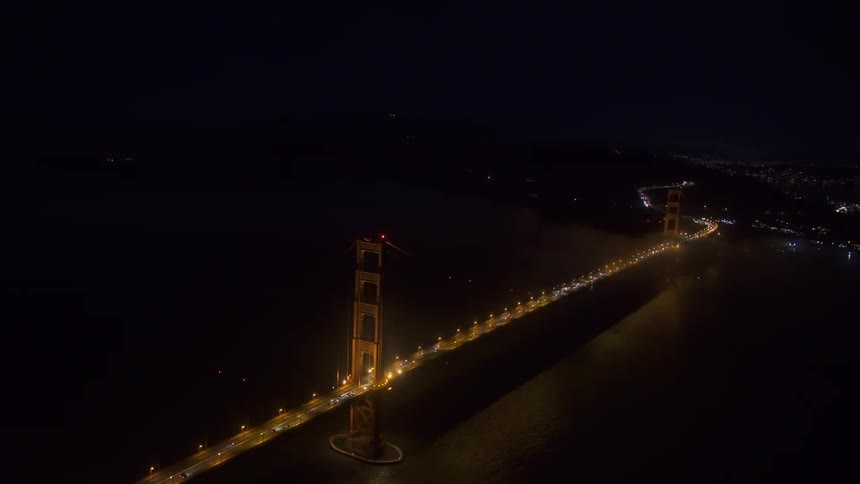 Aerial view of a suspension bridge over a river between near a waterfront city at night