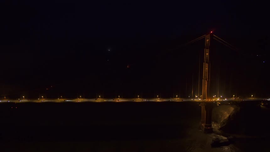 Aerial of commuters driving across a lighted bridge at night