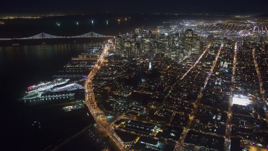 An aerial view of a city skyline on the coast with boats docked and cars driving down streets