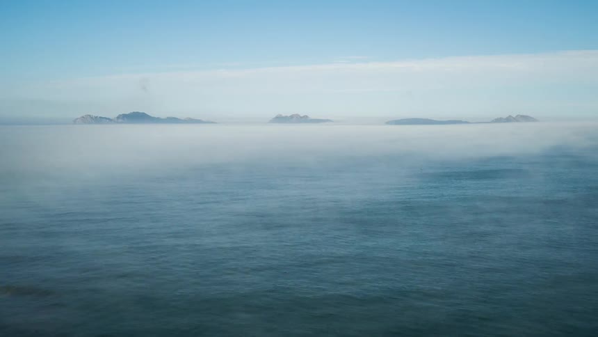 Fog flows over the ocean on a sunny day