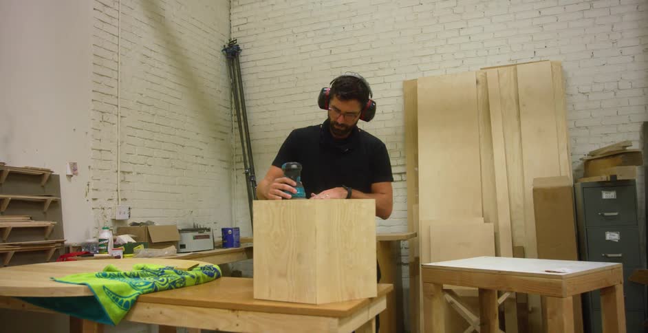 A man works on a wooden block on a workbench in a workshop