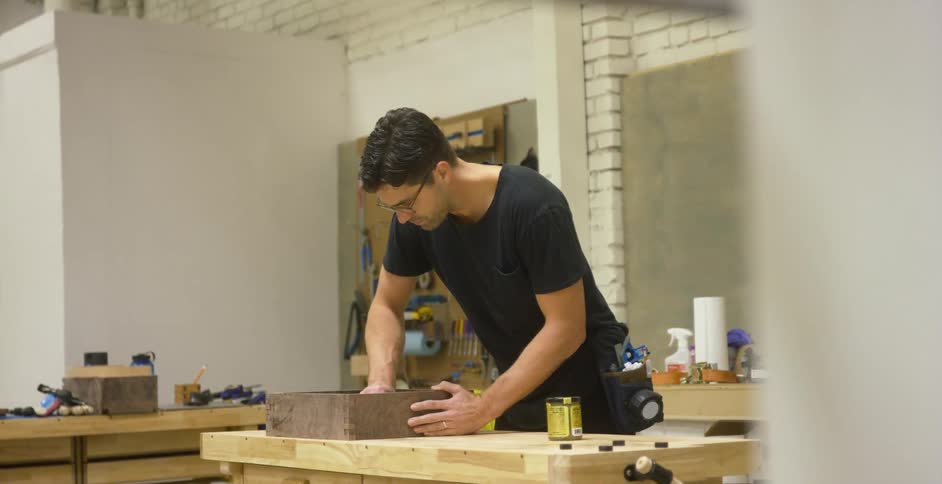 A man working on a piece of wood on a work bench inside of a workshop