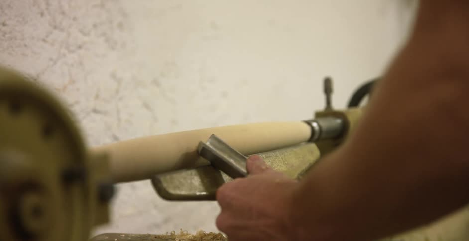 Man carving a piece of hardwood on a lathe in a workshop